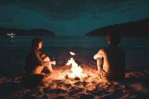 Man and woman sitting next to a bone fire near the beach