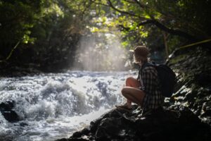 a woman sitting on a stone near the river