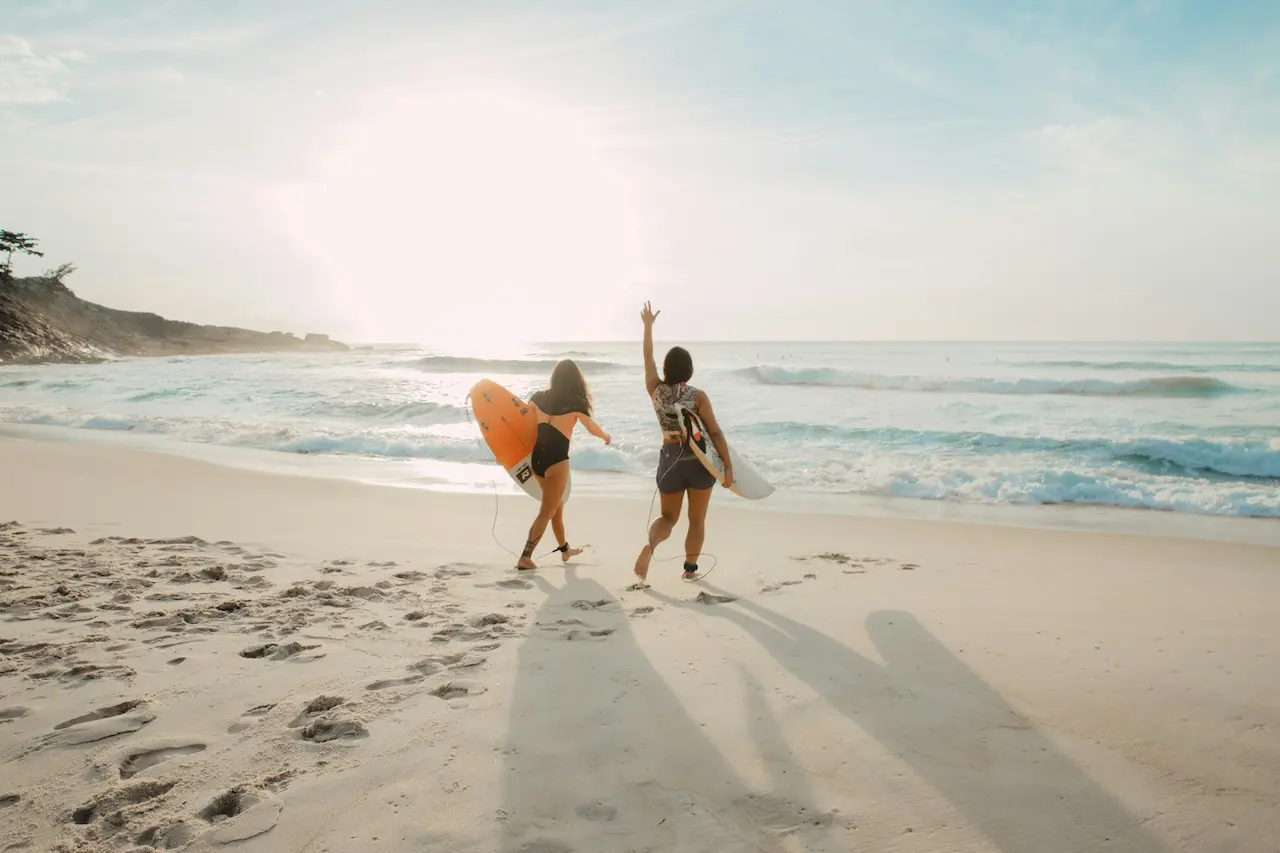 Two Women Walking Toward the Ocean with Surfboards